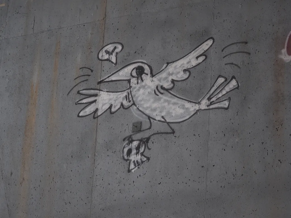 graffiti on a bridge: a bird carrying a skull