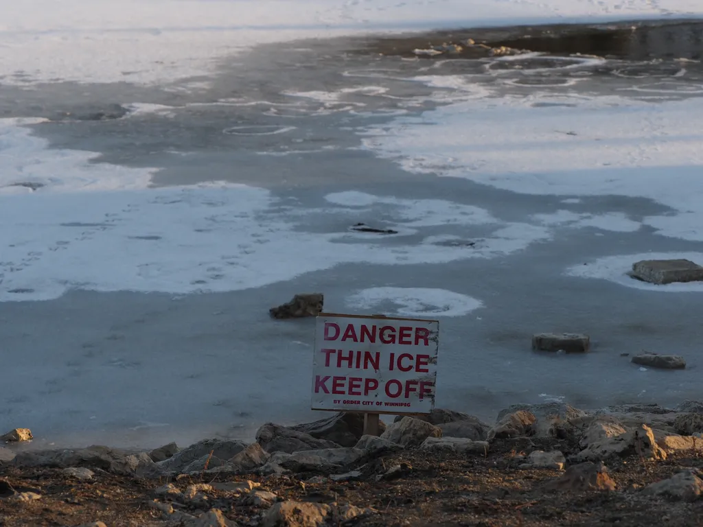 a sign warning of thin ice by a river