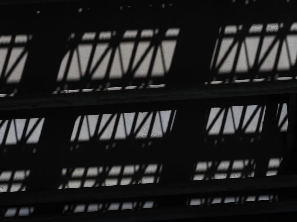 the grating of a bridge casting a shadow on the beams underneath