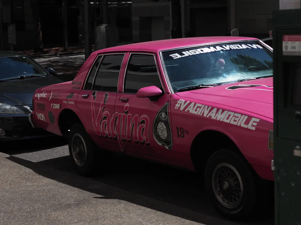 a side view of a pink car with vagina beauty pagent 2024 written on its side and festooned with sponsor logos